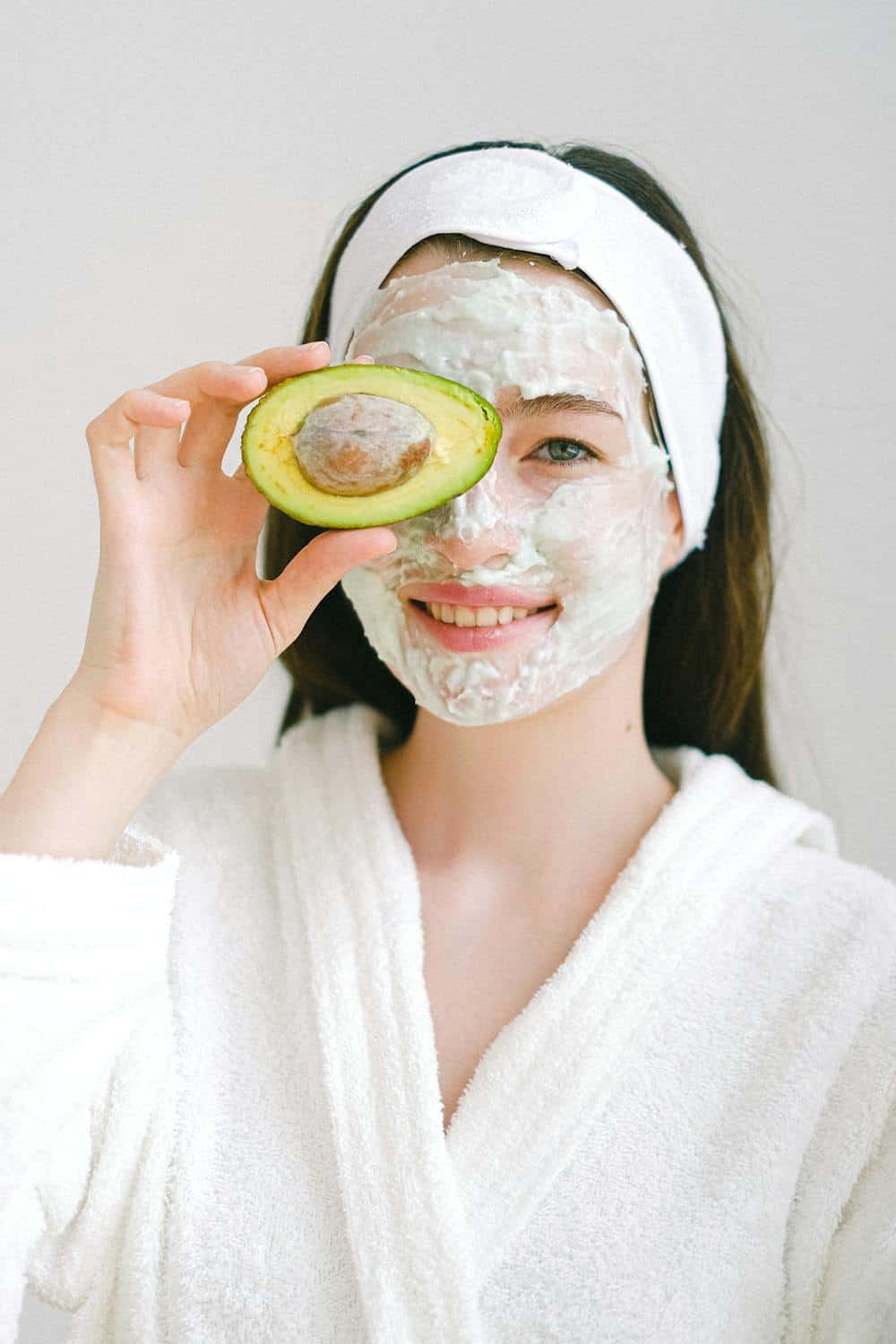 Cheerful woman with face mask made from freeze dry avocado for health and beauty with avocado half over right eye