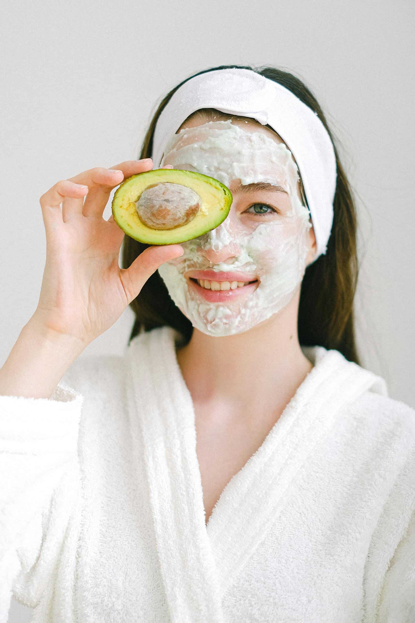 Cheerful woman with face mask made from freeze dry avocado for health and beauty with avocado half over right eye